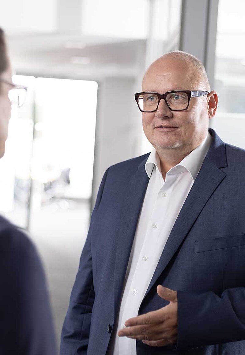 Sven Hemmerle im konzentrierten Austausch mit Kanzlei-Partner im Flur